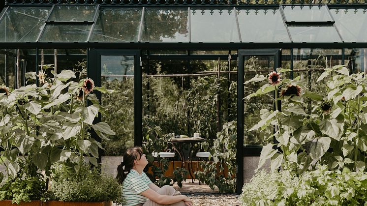 Johanna njuter utanför sitt Helios Unik – ett växthus som förenar odlingsglädje och avkoppling på prästgården i Jäla.