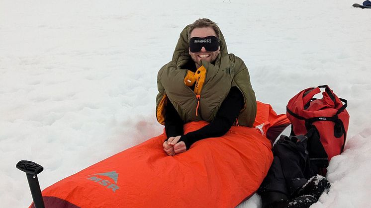 A man sits up in a bivvy bag, he's smiling with a   blackout eye mask for 24 hour daylight! 