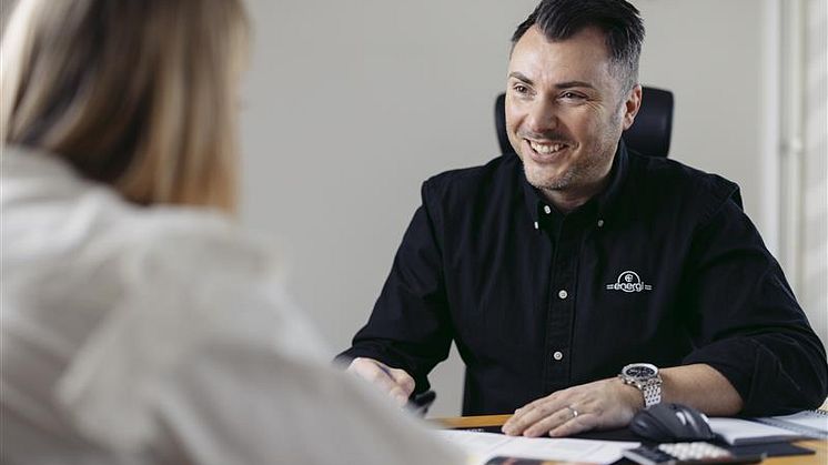En man i C4 Energi-skjorta sitter vid ett skrivbord och talar med en kvinna.