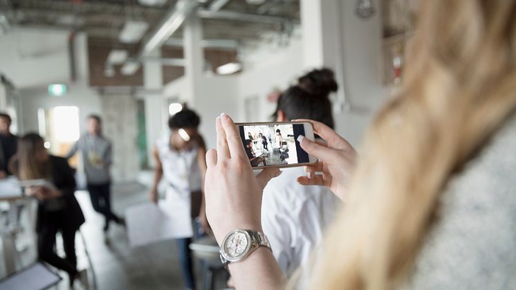 Creative businesswoman with camera phone videoing meeting in office