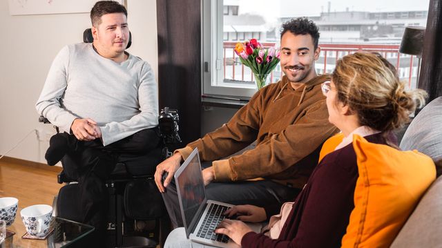 Personer sitter tillsammans och pratar. En person skriver på laptop. De är glada. En person är rullstolsburen. 