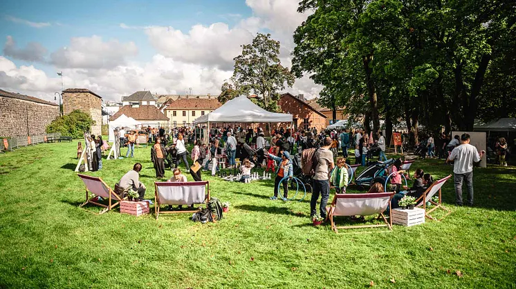 Folkemengde utendørs i solen på gressplen ved festning.