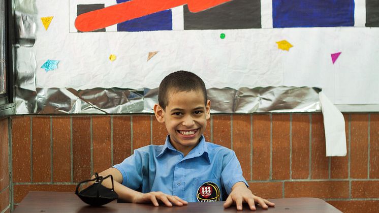 Juan Pablo, 12, från Venezuela sitter och ler vid sin skolbänk.