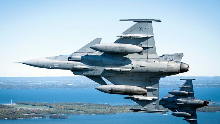 JAS 39 Gripen som flyger över ett område med vindkraftverk. Foto: Antonia Sehlstedt/ Försvarsmakten