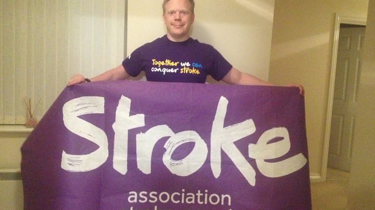 Richard Gillard in a Stroke Association purple top, holding a purple Stroke Association flag. 