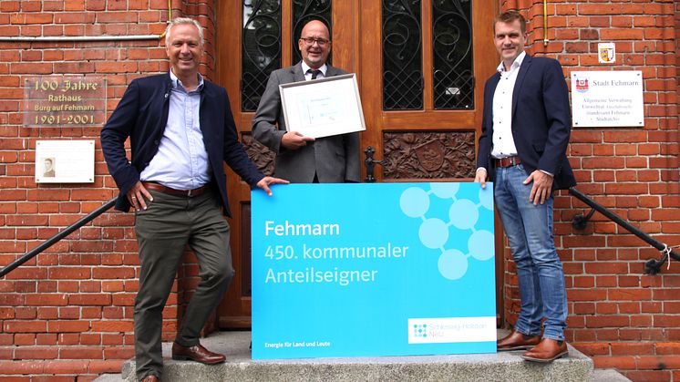 Foto: SH Netz - Symbolische Aktienübergabe vor dem Rathaus (v.l.) Matthias Boxberger, Aufsichtsratsvorsitzender bei SH Netz, Bürgermeister Jörg Weber und Mirko Sadowski, Leiter des Technik-Standortes von SH Netz im Kreis Ostholstein.