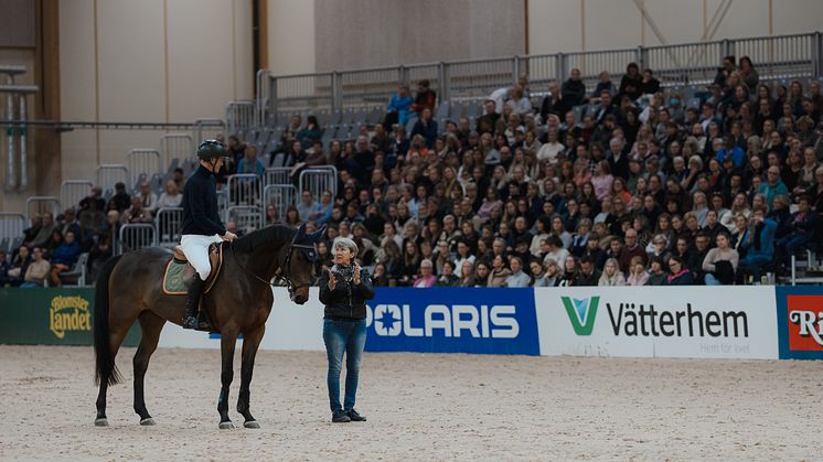 Kyra Kyrklund tillsammans med Peder Fredricson och Raadbjergs’s Bahia under clinicen på Jönköping Horse Show. Med hjälp av sin berömda fjäder illustrerar Kyra hästens rörelse vid ridning. 