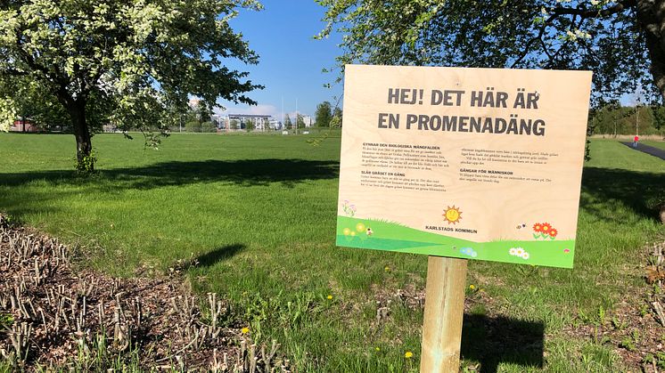 Skylt om promenadäng vid grönyta på Orrholmen.
