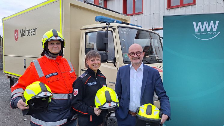 Christian Weidlich, stv. Stadtbeauftragter, Stefanie Friemuth, Stadtbeauftragte und Andreas Speith, Westfalen Weser Netz Geschäftsführer mit den neuen Schutzhelmen vor einem Einsatzfahrzeug der Malteser. (Foto: Westfalen Weser)