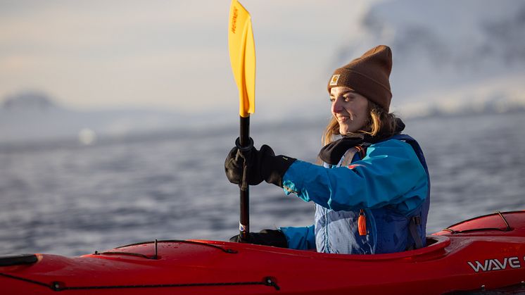 A solo women paddles in Antarctica's Orne Harbour in a hard shell kayak.