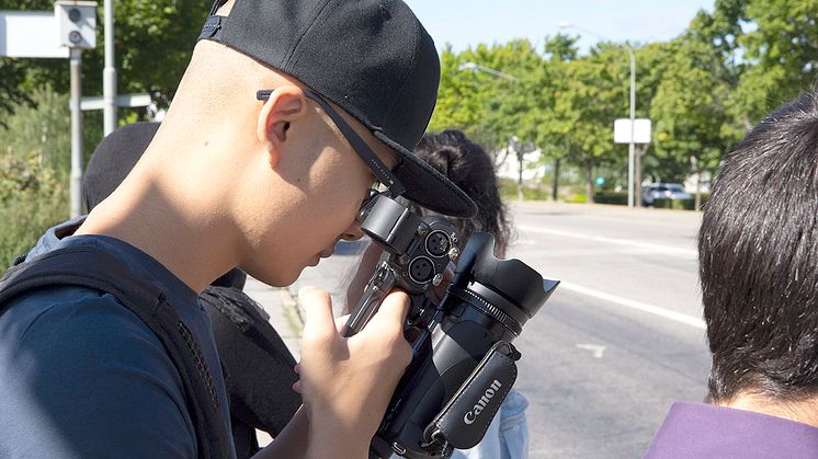 Syntolkning: Ungdomar utomhus vid en väg, en håller i och tittar in i en filmkamera. Foto: Mikael Ström