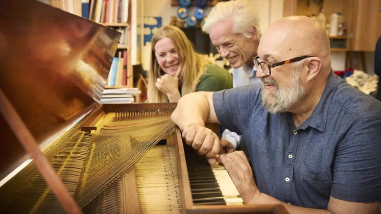 Två män och en kvinna sitter framför ett gammalt piano