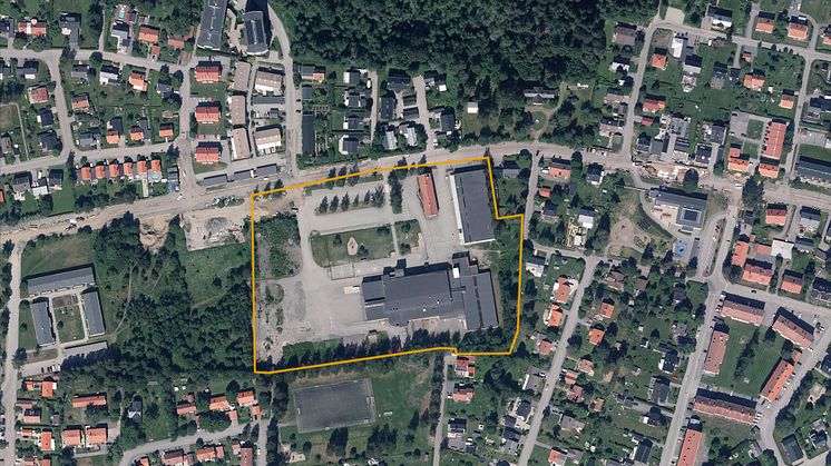 Flygfoto över ett bostadsområde med en markerad yta i gult som visar planområdet kring en större byggnad och skolgård.