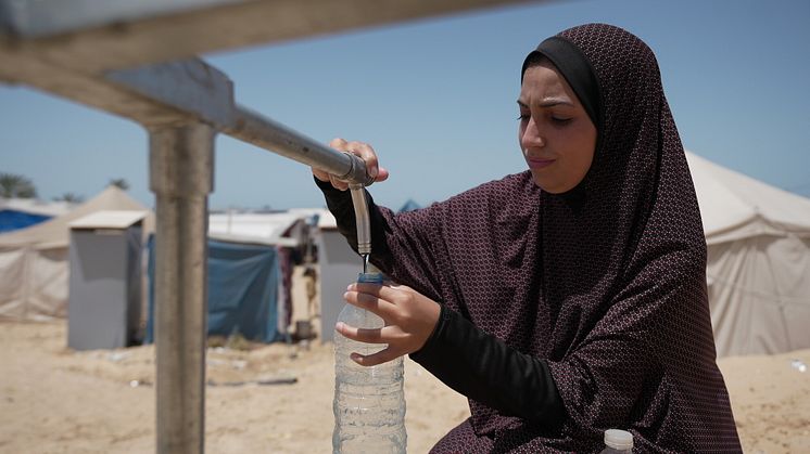 Duaa Abu Sabha fyller på vattenflaskor från Oxfams vattentank, som installerats i Al-Malwasi, Gaza. Foto: Alef Multimedia/Oxfam