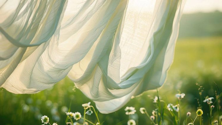 Vitt tyg som fladdrar i vinden med en blomäng som bakgrund