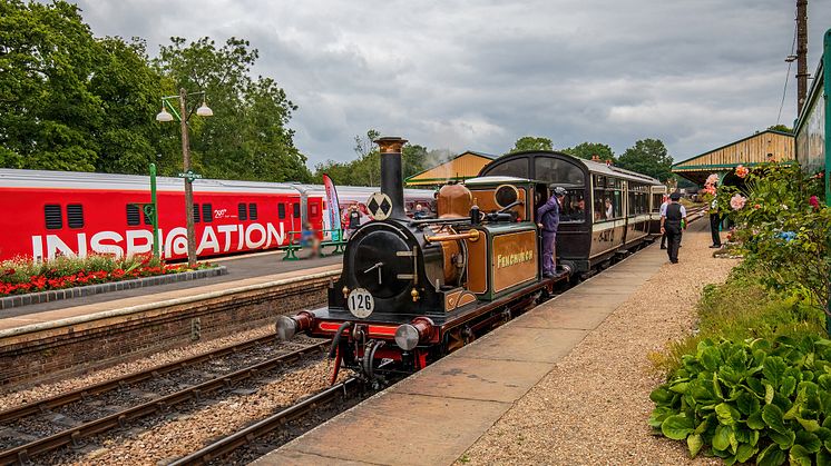 A steam train stands in a platform on the Bluebell Railway next to the red modern day exhibition train named Inspiration