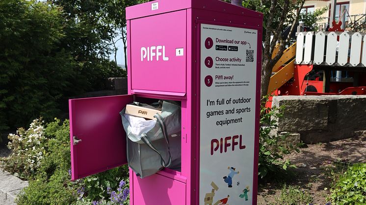 Piffls rosa aktivitetsbox i en blommande park i Strömstad, med en öppen lucka som visar en tygpåse fylld med utomhusspel och klossar.