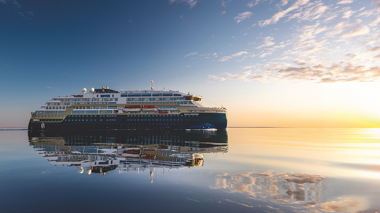 A HX branded ship sails on still water into the sunset. 