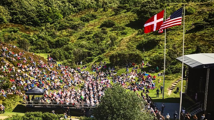 Billede der viser publikum til Rebildfesten. De kigger mod en scene hvor det danske og amerikanske flag vejer.