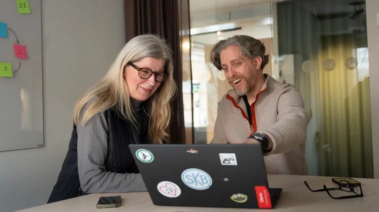 Två glada personer sitter vid en dator och arbetar tillsammans.