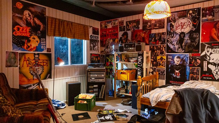 Ett rum med en säng, fåtölj, en elgitarr, skivbackar och hårdrocksaffischer.