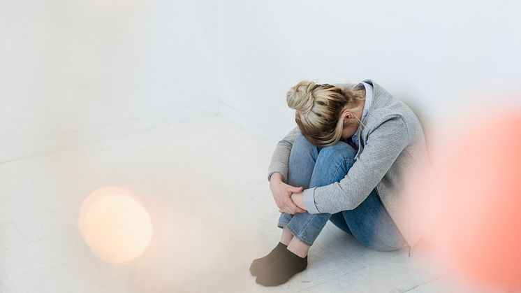 En kvinna sitter ned  på golvet med huvudet nedsänkt