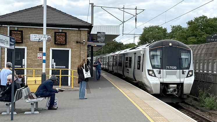 Train 717020 stands in a platform at Finsbury Park station with passengers sitting on benches, waiting for trains