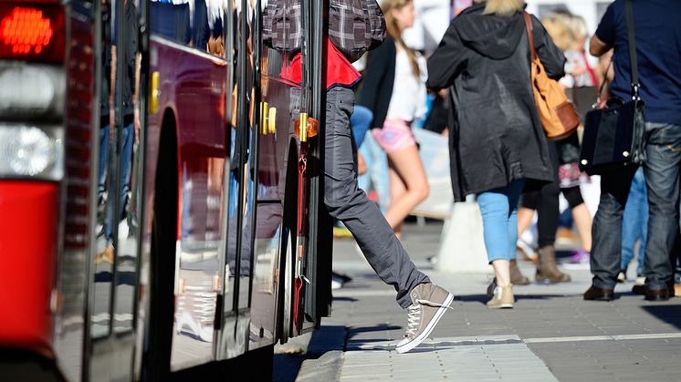 Person kliver på en buss, flera resenärer ses i bakgrunden.