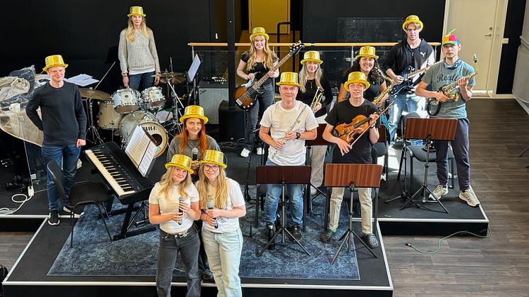 En grupp unga människor med gula hattar står på en scen med med notställ och varsitt instrument.