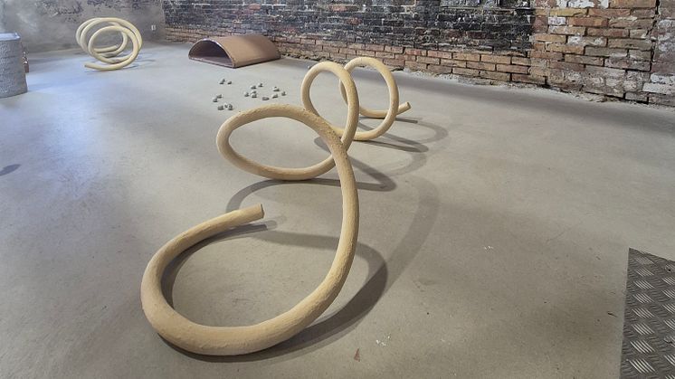 Två stora spiralformade konstverk på ett grått stengolv i en öppen sal med en tegelvägg i bakgrunden.