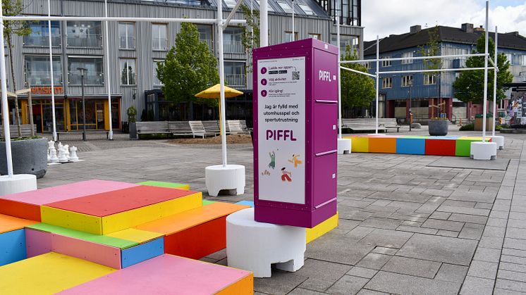 Pifflbox är placerad på ett torg i Kungsbacka, omgiven av färgglada trälådor i olika nivåer som fungerar som sitt- och lekyta, som ett stort schackspel, vilket skapar en levande och tillgänglig plats för rörelse och lek.
