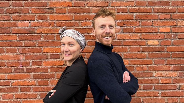 Projektledare Märta Lindqvist Weddig och projektkoordinator Martin Lilja ler in i kameran, de står framför en röd tegelvägg