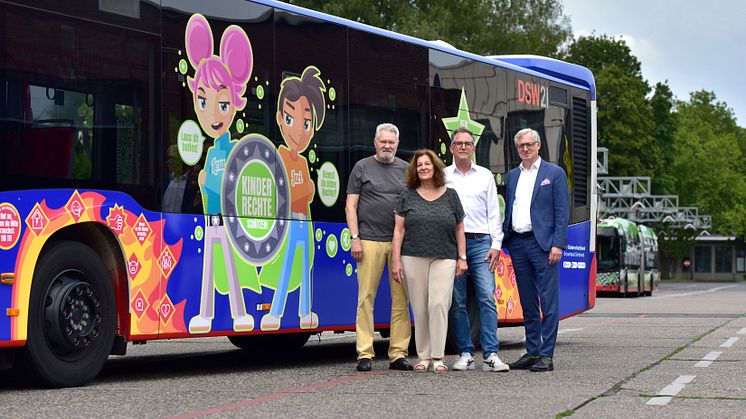 Bunt beklebter Linienbus mit vier Personen davor. Der Bus fährt für die Rechte der Kinder in Dortmund als rollende Werbung.