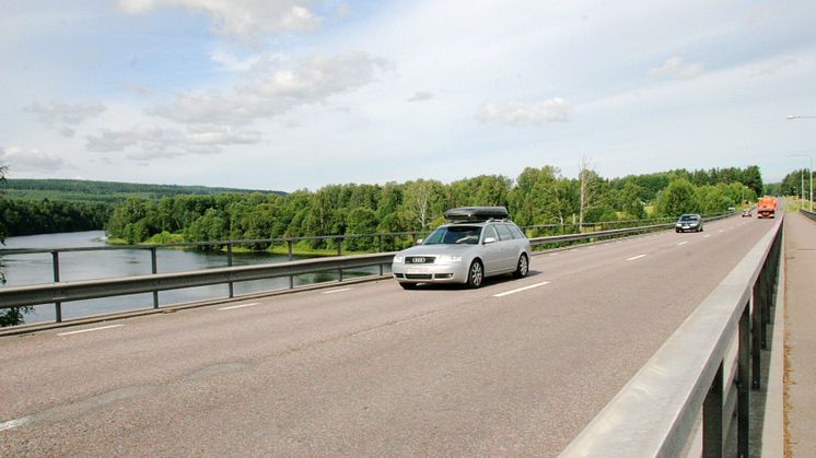 Personbilar kör på en bro i sommarväder. 