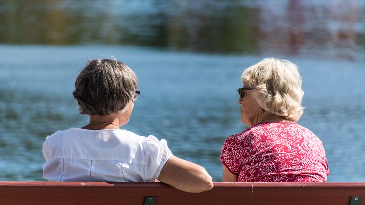 Två äldre kvinnor sitter på en bänk och samtalar och tittar ut över vattnet.