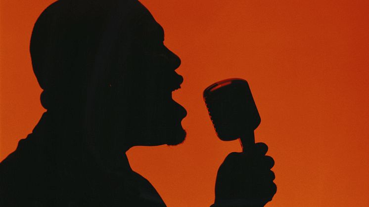 Siluetten av en man i profil, som sjunger eller pratar i en mikrofon av äldre typ. Illustration.