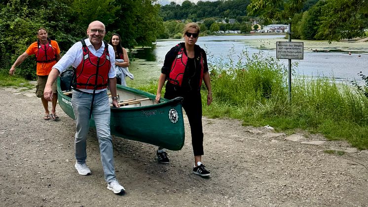 Ein Mann und eine Frau tragen ein Kanu zum Wasser. Axel Biermann von Ruhr Tourismus und NRW-Wirtschaftsministerin Mona Neubau