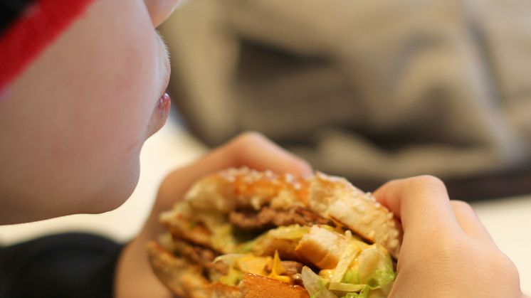 Bilden föreställer en pojke som äter en hamburgare