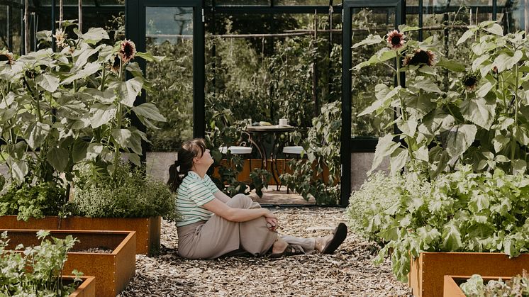 Johanna njuter utanför sitt Helios Unik – ett växthus som förenar odlingsglädje och avkoppling på prästgården i Jäla.