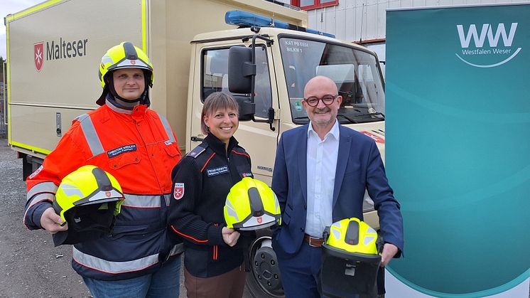 Christian Weidlich, stv. Stadtbeauftragter, Stefanie Friemuth, Stadtbeauftragte und Andreas Speith, Westfalen Weser Netz Geschäftsführer mit den neuen Schutzhelmen vor einem Einsatzfahrzeug der Malteser. (Foto: Westfalen Weser)