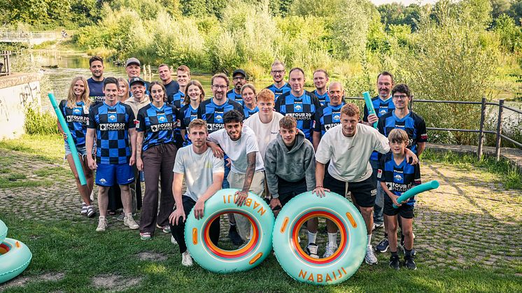 Auf dem Foto sind 25 Personen zu sehen, die in die Kamera lächeln. Die Menschen in der ersten Reihe halten Schwimmreifen.