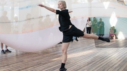 Kvinnlig dansare dansar framför publik i ett rum med takfönster och tyg som hänger från taket