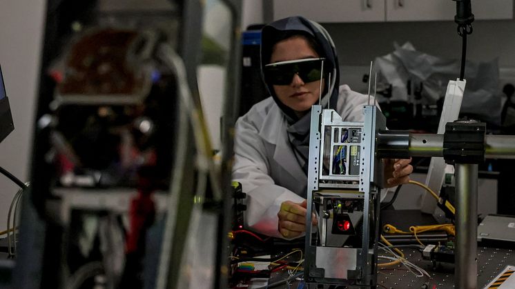 a scientist is pictured in a lab with a metal cubesat with a red laser