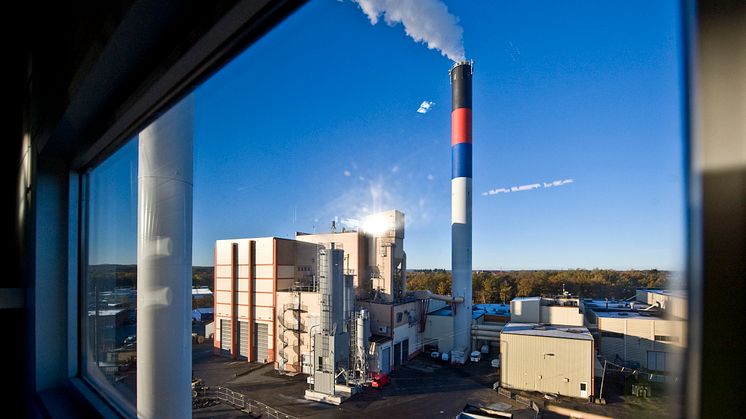 Fjärrvärmeverket i Hässleholm sett på håll. Gul industribyggnad med rykande skorsten.