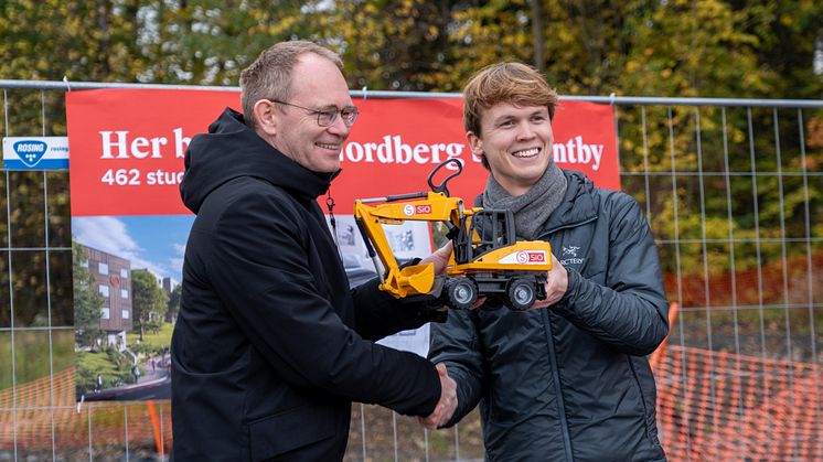 Statsråd Oddmund Hoel mottar en gravemaskin fra student og styreleder i SiO, Eilif Tanberg,  som påminnelse om at SiO er klare til å sette spaden i jorda på nye studentboligprosjekter.  