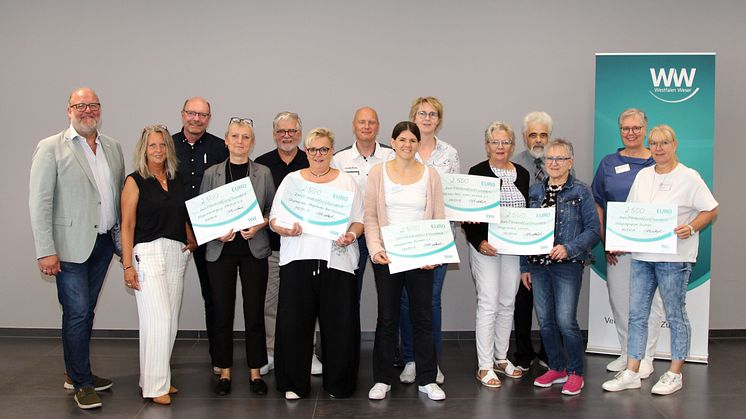 Vertreter*innen der begünstigten Hospizinitiativen stehen in einer Reihe und halten symbolisch überreichte Schecks.