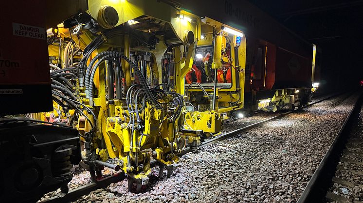 A bright yellow machine works on the track at night