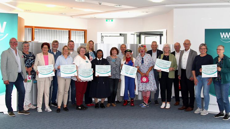 Vertreter*innen der begünstigten Hospizinitiativen stehen in einer Reihe und halten symbolisch überreichte Schecks.