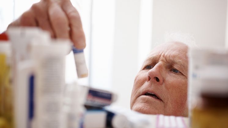 Äldre man tar medicinflaska från en hylla