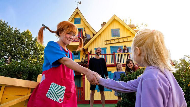 Pippi Långstrump hälsar på ett barn framför Villa Villekulla